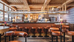 Un restaurant avec des poutres en bois au plafond, des tabourets de bar et un coin bar où sont suspendus des verres.