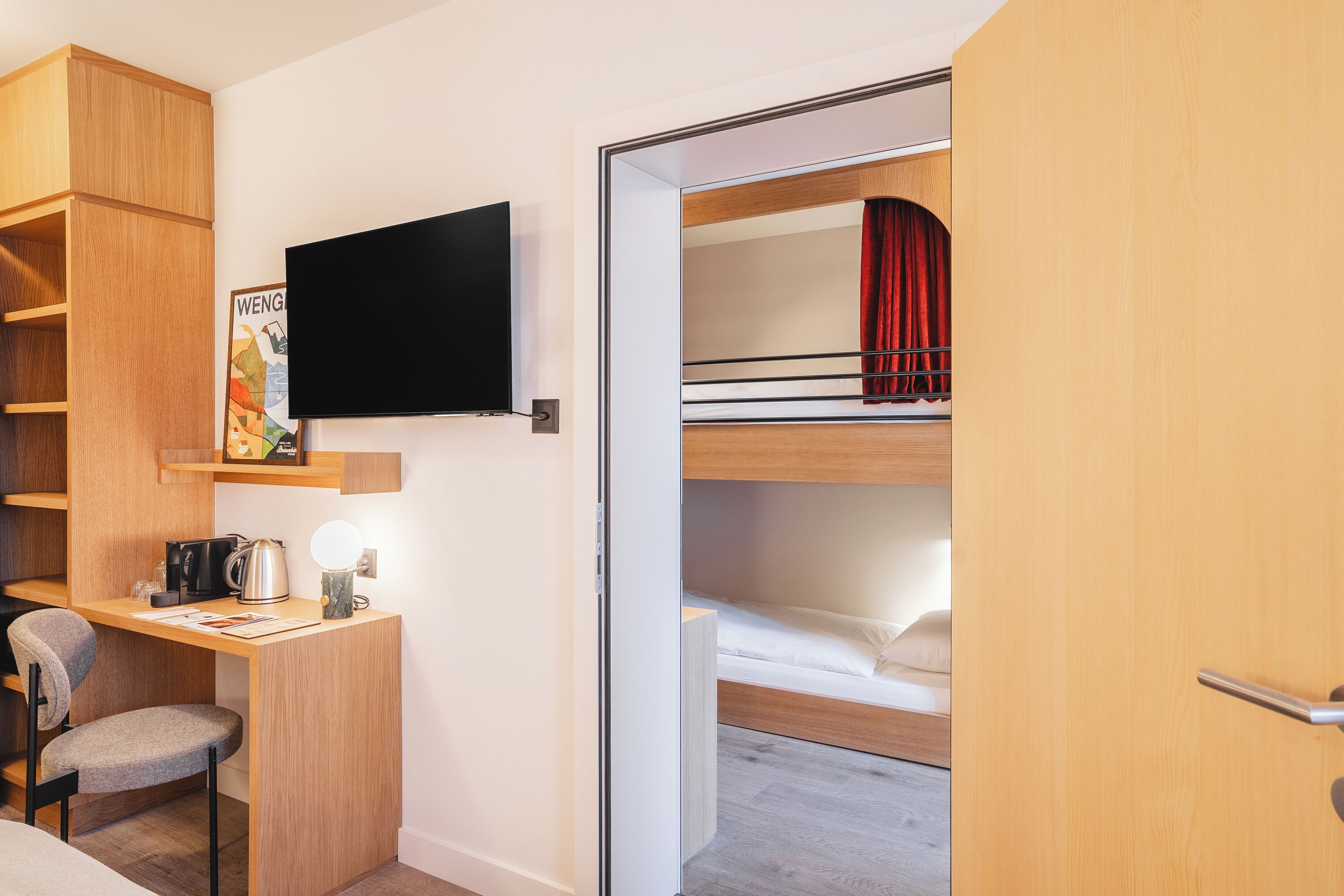Ein kompaktes Hotelzimmer mit Etagenbett, Schreibtisch mit Stuhl, Fernseher und einer kleinen Küchenzeile.