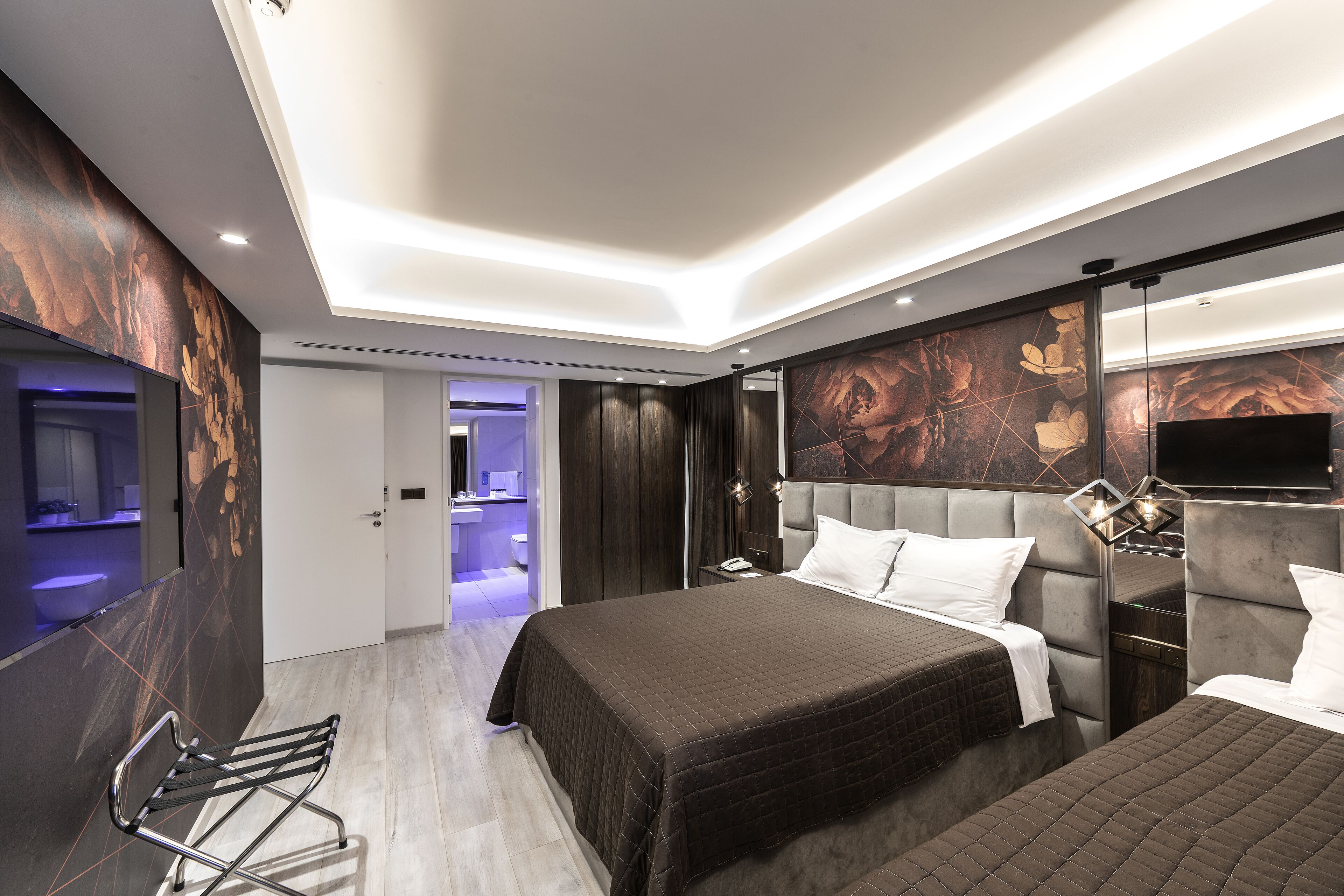 A modern hotel room with a large bed, a bedside table, a flat-screen TV, and a bathroom visible through an open door.
