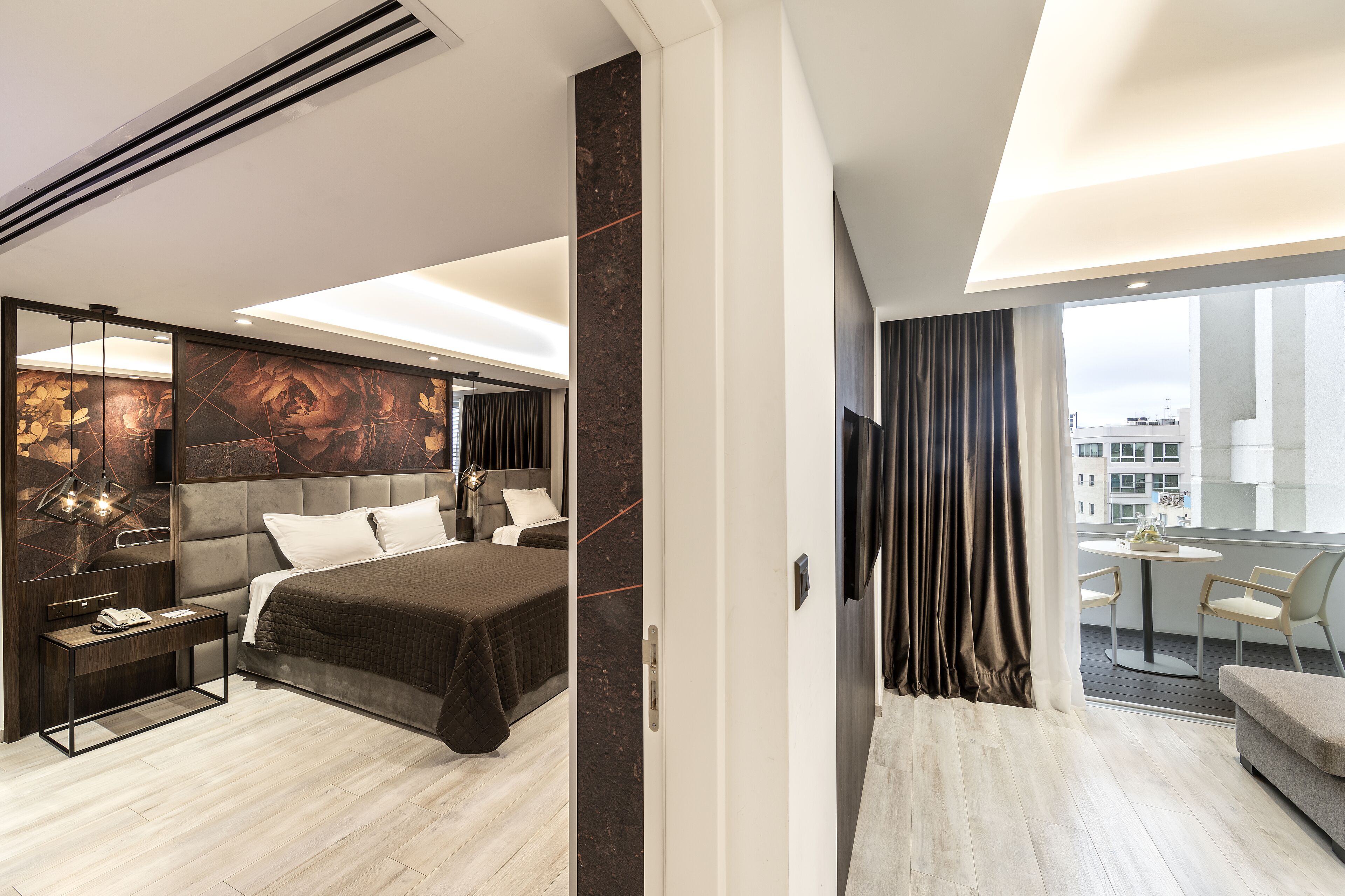 Een moderne hotelkamer met een groot bed, een nachtkastje, een bureau en een balkon met een tafel en stoelen.