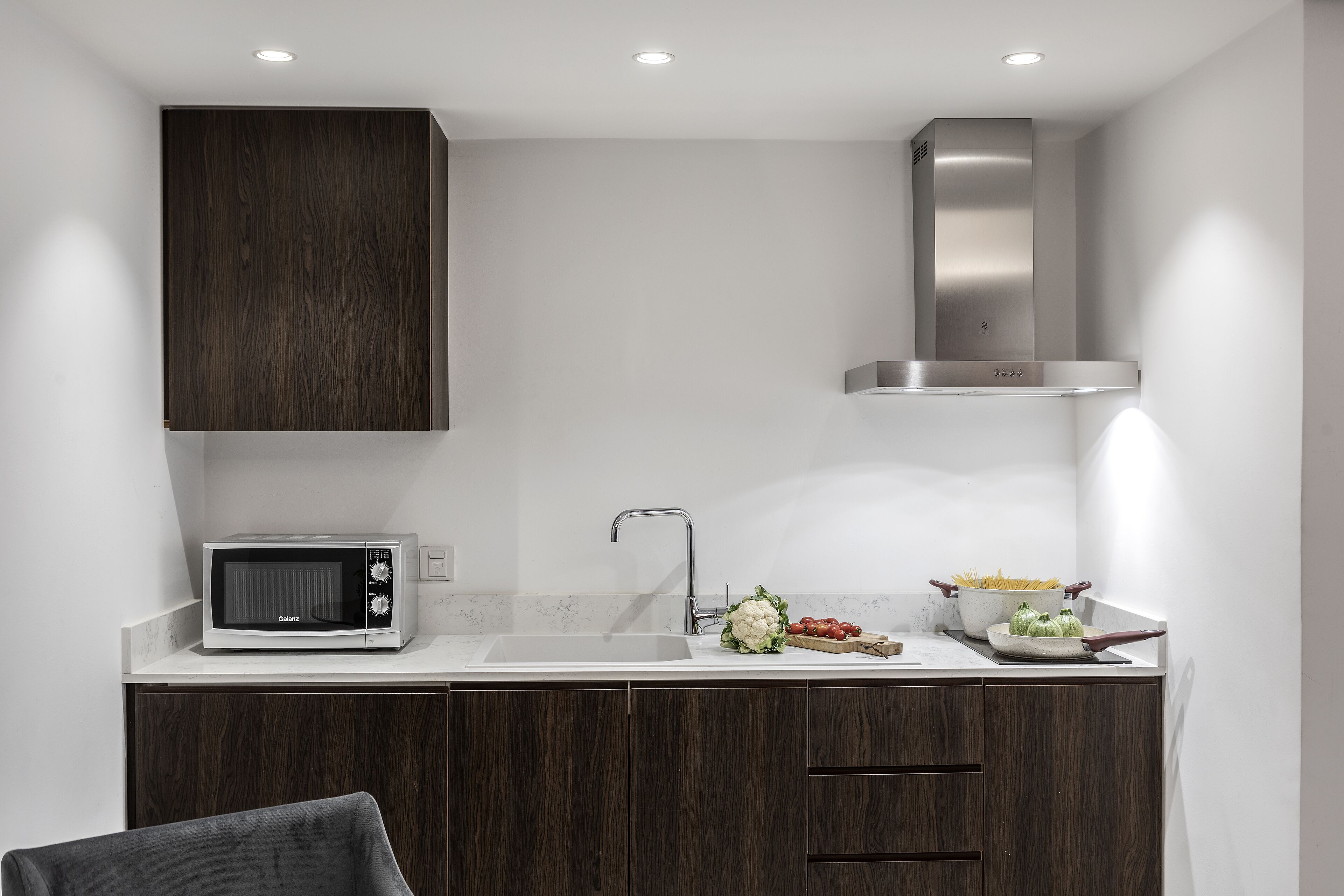 A modern kitchen with dark wood cabinets, a stainless steel range hood, a built-in microwave, and a sink.
