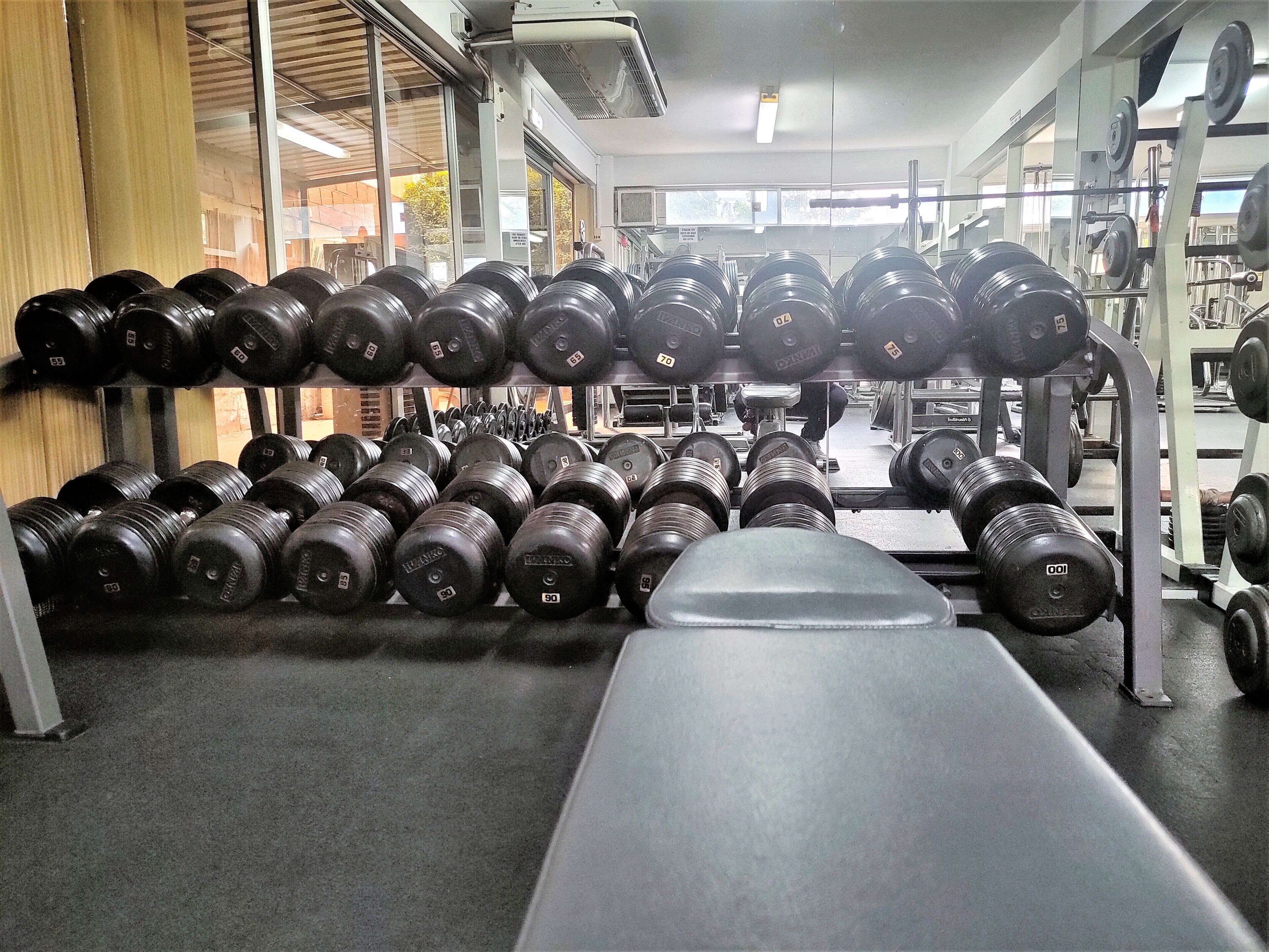 A gym with rows of black dumbbells and weight plates, a bench, and various exercise equipment.