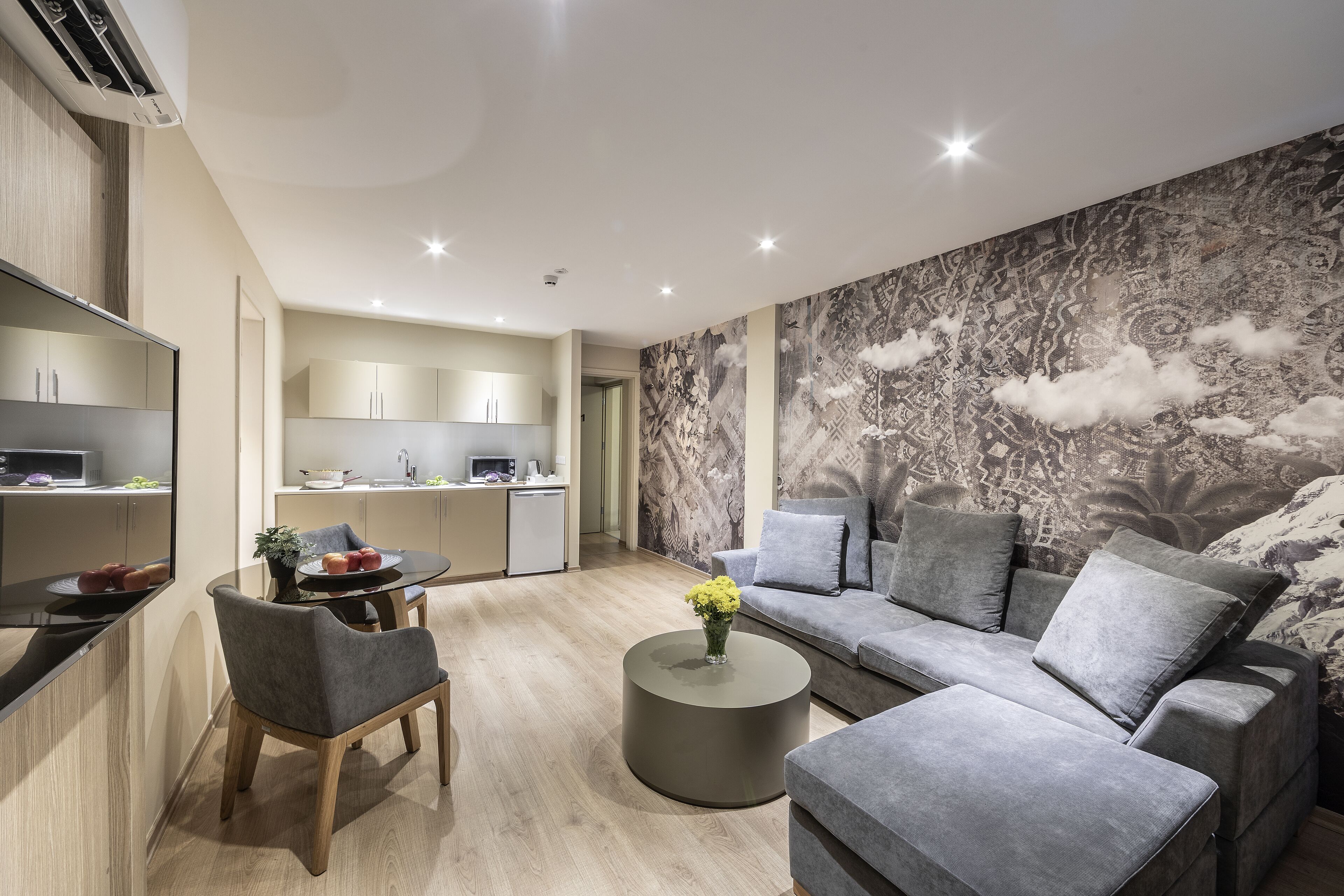 A modern living room with a grey sofa, a round coffee table, and a dining area with a small table and chairs.