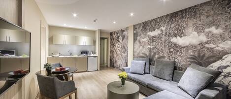 A modern living room with a grey sofa, a round coffee table, and a dining area with a small table and chairs.