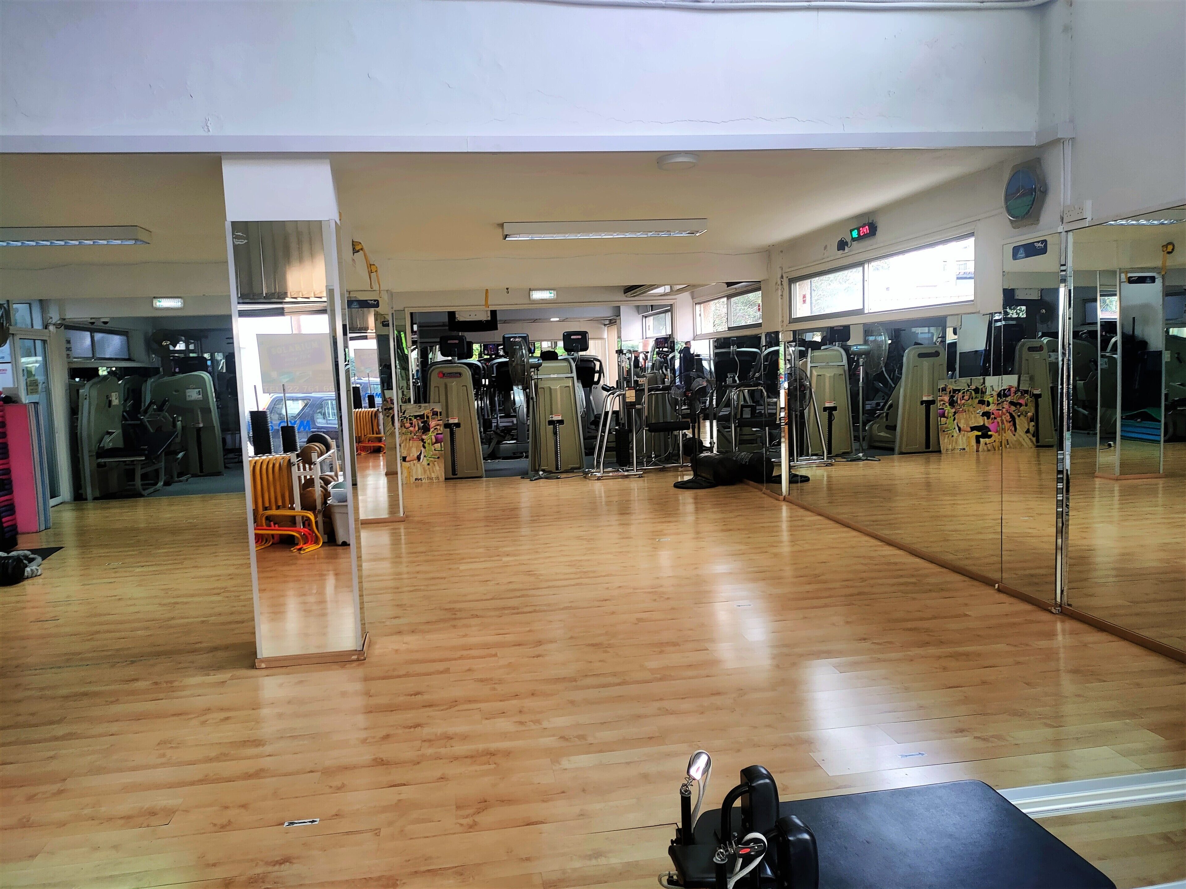 A gym with various exercise machines, a wooden floor, and a large mirror wall.