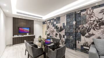 Quarto moderno com mesa de jantar de vidro, cadeiras estofadas cinzentas, televisão de tela plana e parede decorativa com azulejos florais.