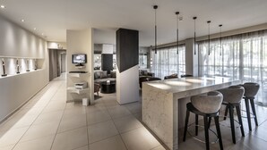 Une cuisine moderne dotée d’un plan de travail en marbre et de tabourets de bar, un coin repas avec un canapé et une table, et de grandes fenêtres qui laissent entrer la lumière naturelle.