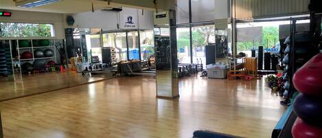 A gym with wooden floors, exercise equipment, and a large mirror.