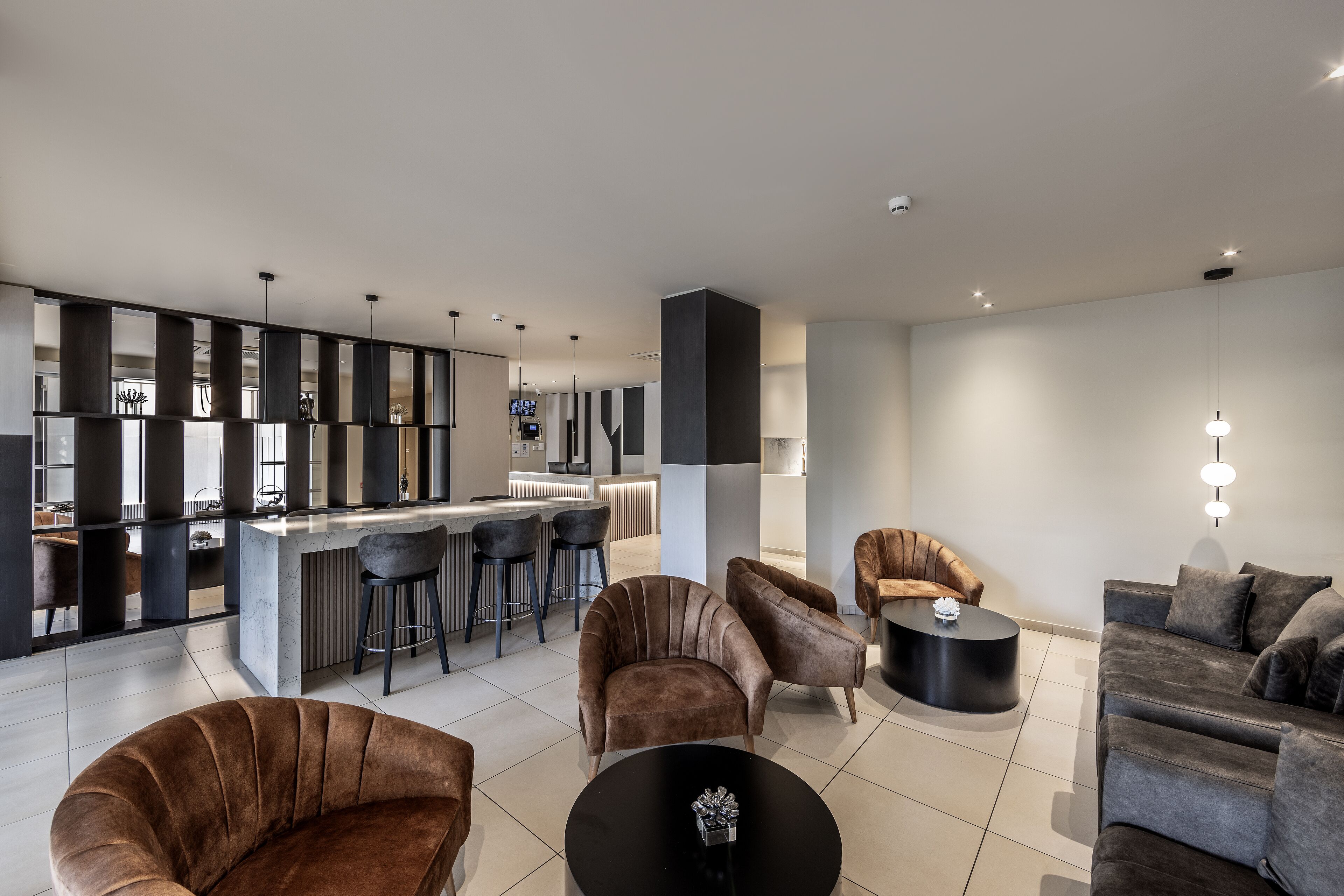 A modern living room with a bar area, brown upholstered chairs, a black round table, and a grey sofa.