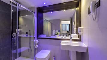 A modern bathroom with a glass-enclosed shower, a white toilet, a sink, and a mirror with a telephone.