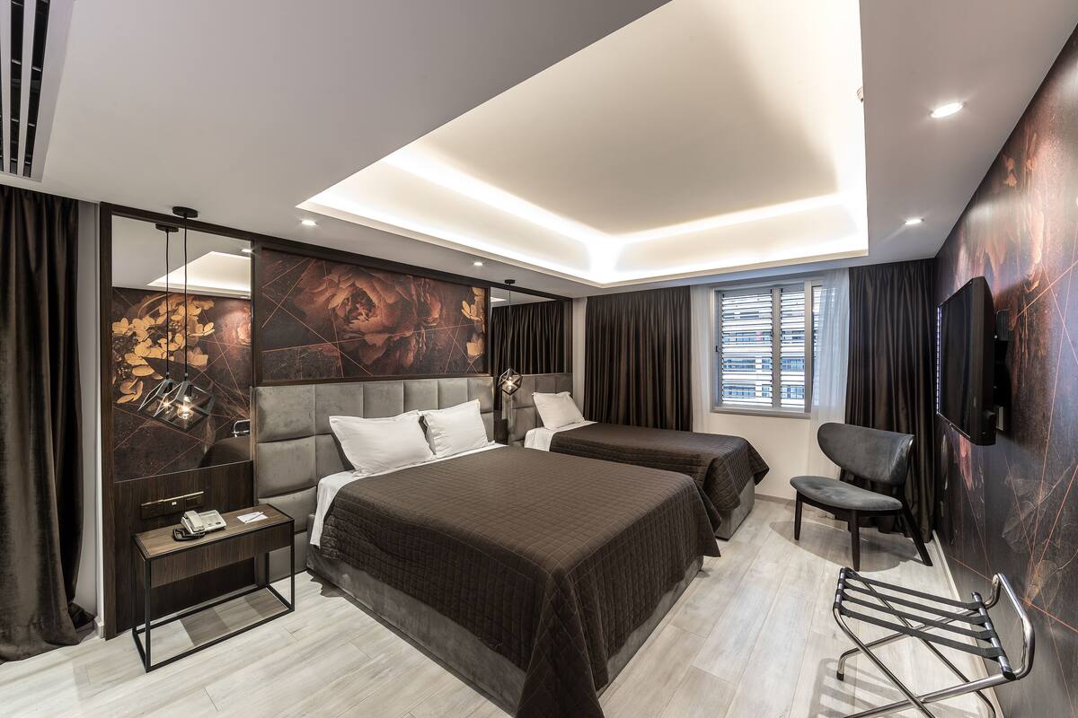 A modern hotel room with two beds, a desk, a chair, and a TV.