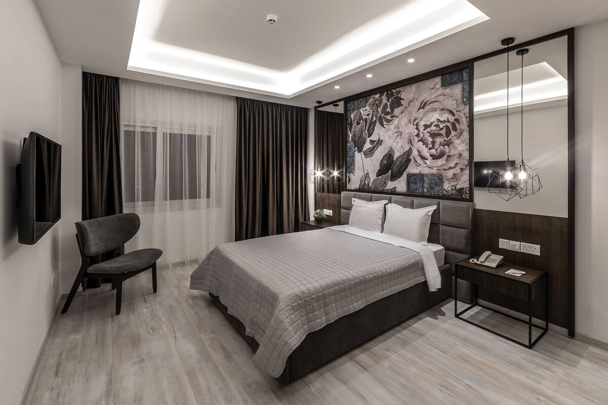 A modern bedroom with a large bed, a chair, a bedside table with a phone, and a wall-mounted TV.