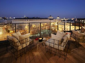 Eine Dachterrasse mit Blick auf Stadtgebäude, ausgestattet mit Stühlen und einem kleinen Tisch.