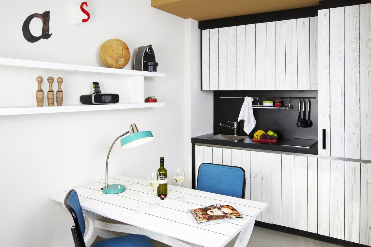 A compact kitchen with white cabinetry, a dining table with a blue chair, and a small island with a sink.