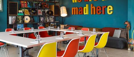 Uma sala de reunião moderna com um grande mural na parede, uma estante com discos de vinil e cadeiras coloridas.