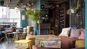 Un coin salon accueillant avec un canapé, une petite table, un tabouret et une valise ancienne.