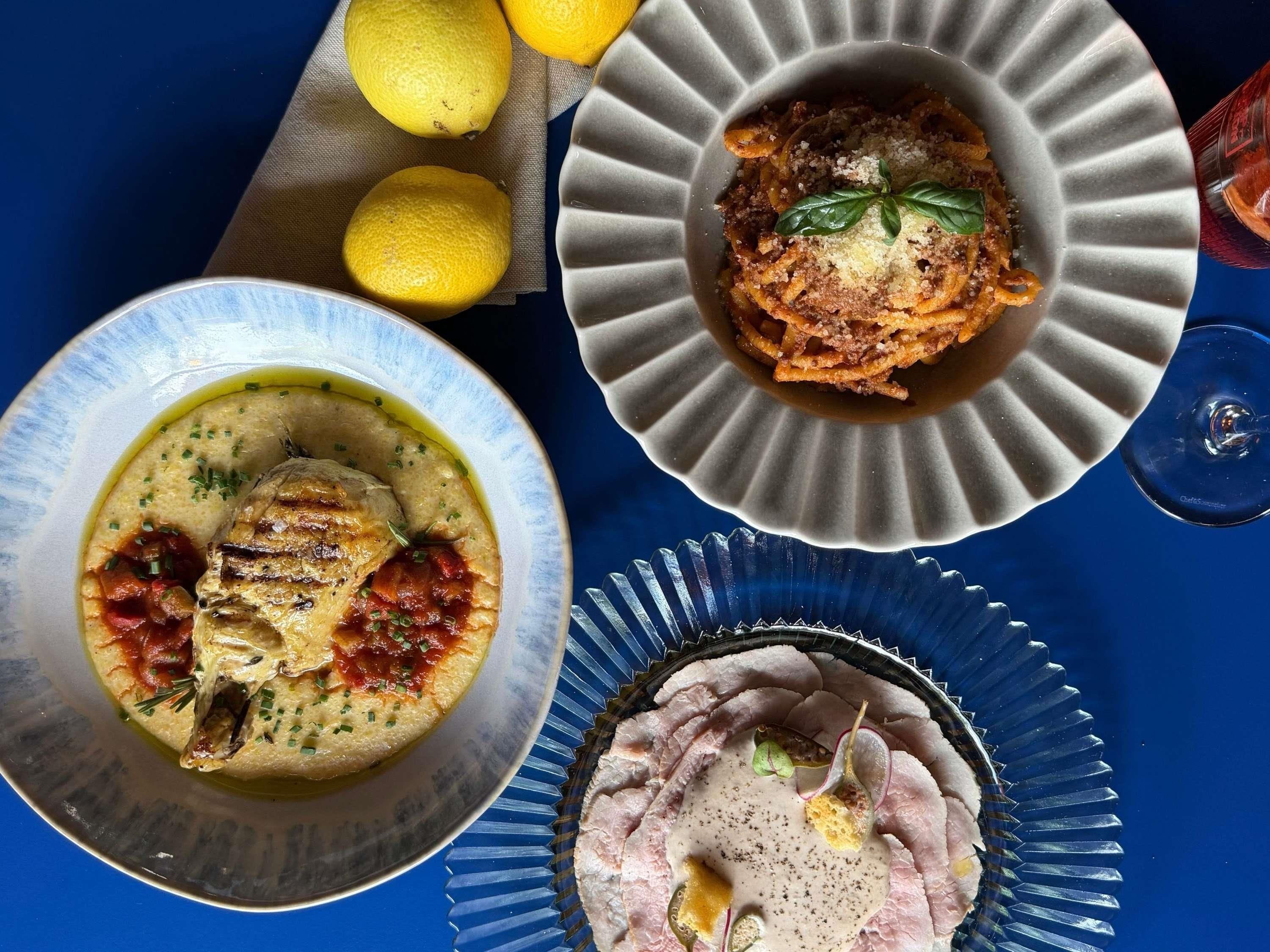 Una mesa con tres platos: una sopa cremosa con hierbas, un plato de pasta con carne y un plato de carne en rodajas con salsa cremosa.