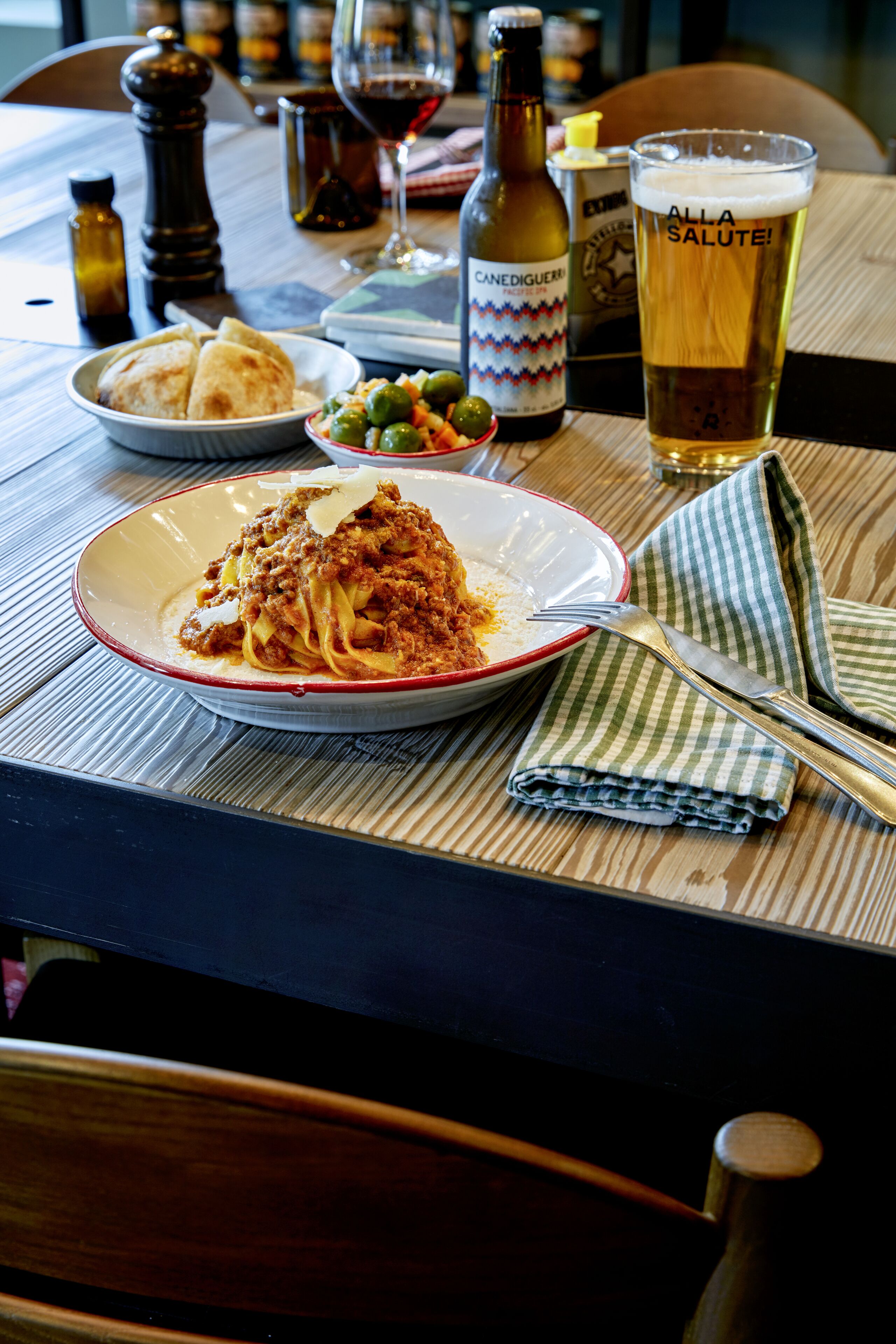 Una mesa de comedor con un plato de espagueti, una jarra de cerveza y una botella de vino.