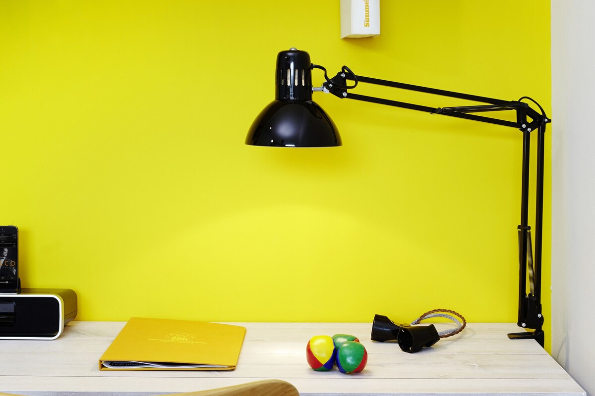 A workspace with a white desk, a black desk lamp, a yellow folder, and a wooden chair.