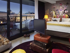 A hotel room with a large window, a television, a bed, a wall mural, and a balcony with a view of a cityscape. - 25hours Hotel Vienna at MuseumsQuartier (Vienna)