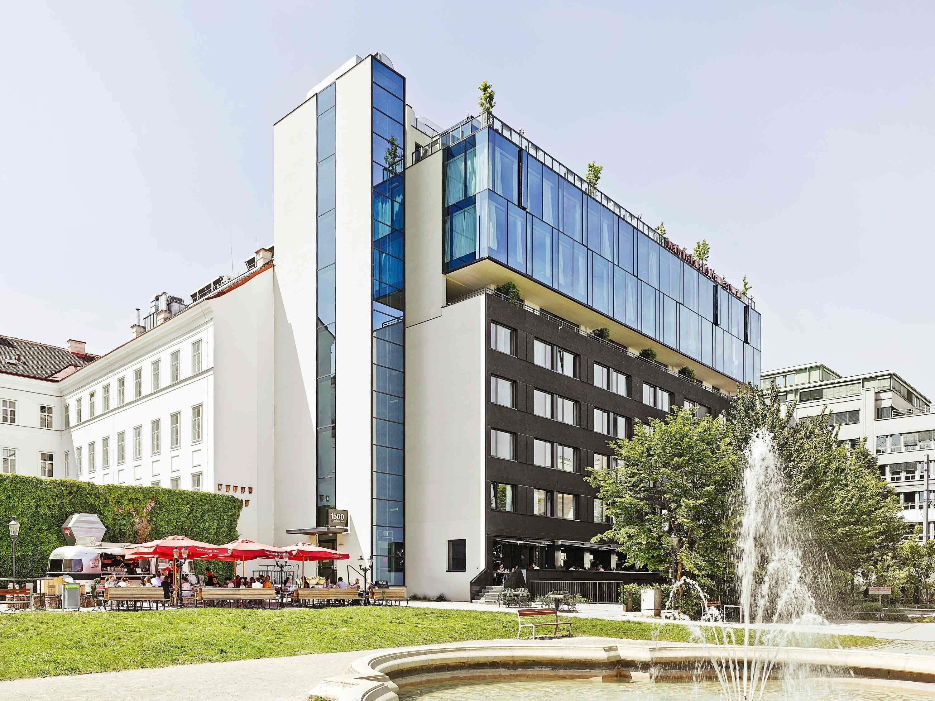 A modern building with a glass facade, a fountain, and outdoor seating with umbrellas.