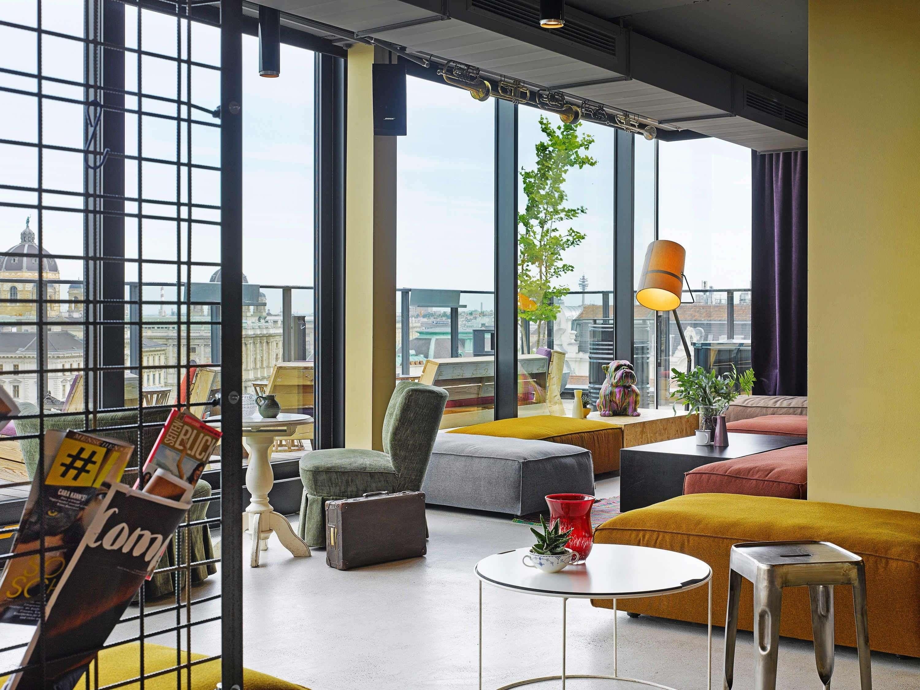 Een moderne woonkamer met grote ramen, uitzicht over de stad en verschillende zithoeken.