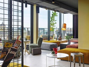 A modern living room with large windows, a city view, and a variety of seating options. - 25hours Hotel Vienna at MuseumsQuartier (Vienna)