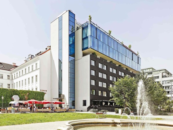 A modern building with a glass facade, a fountain, and outdoor seating with umbrellas.