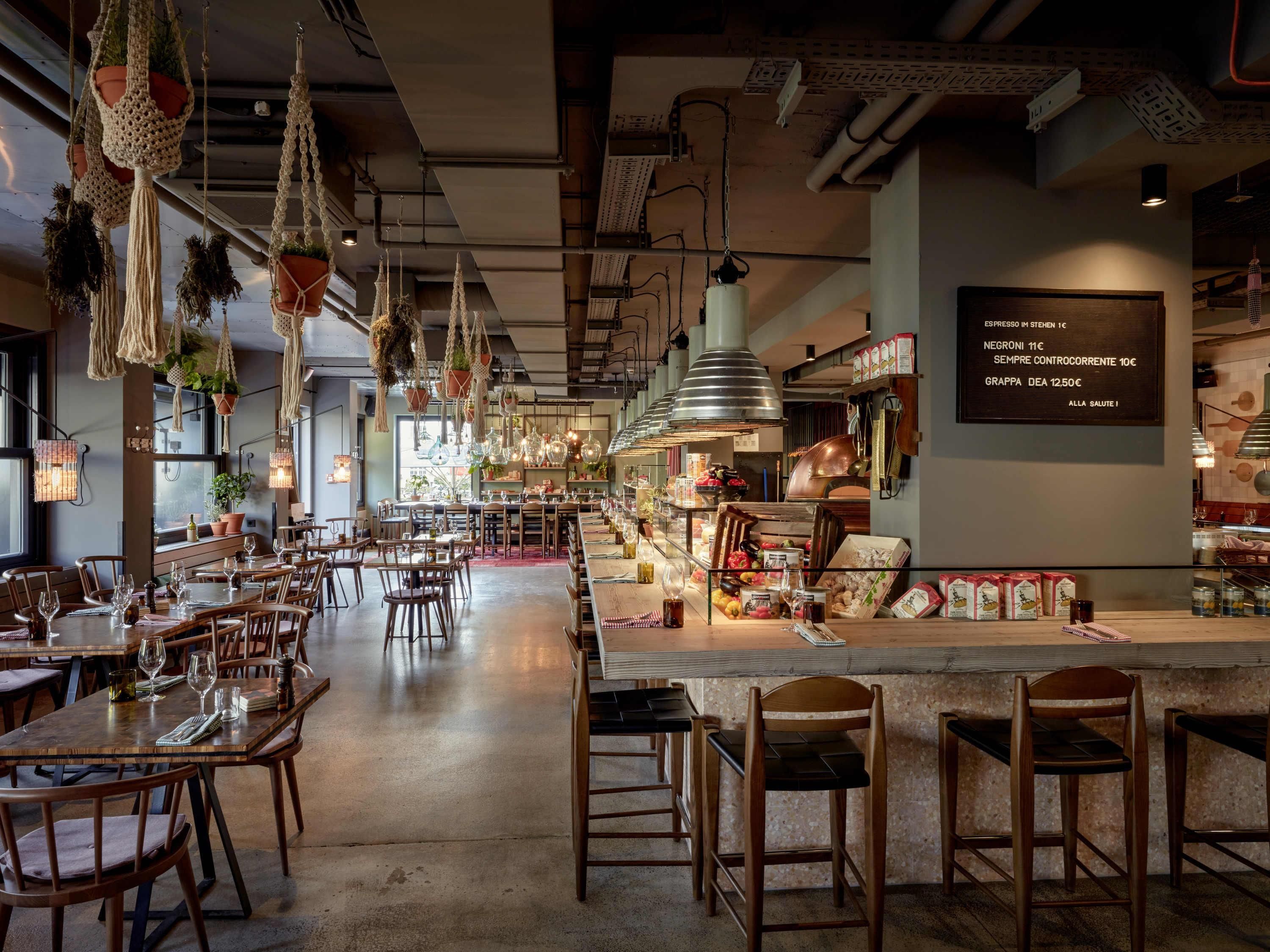 A restaurant interior with hanging macramé planters, wooden tables, and a menu board.