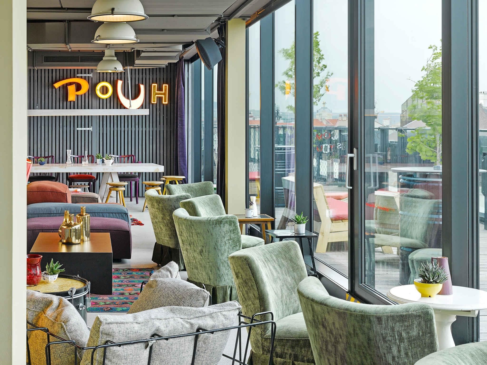 A modern interior with seating, a bar area, and large windows offering city views.