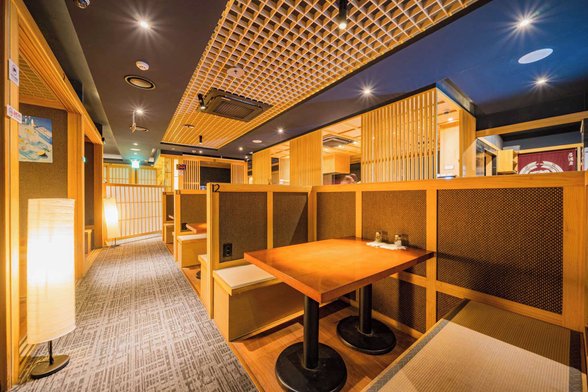 A traditional Japanese-style room with tatami flooring, low wooden partitions, and a table with a cushion.