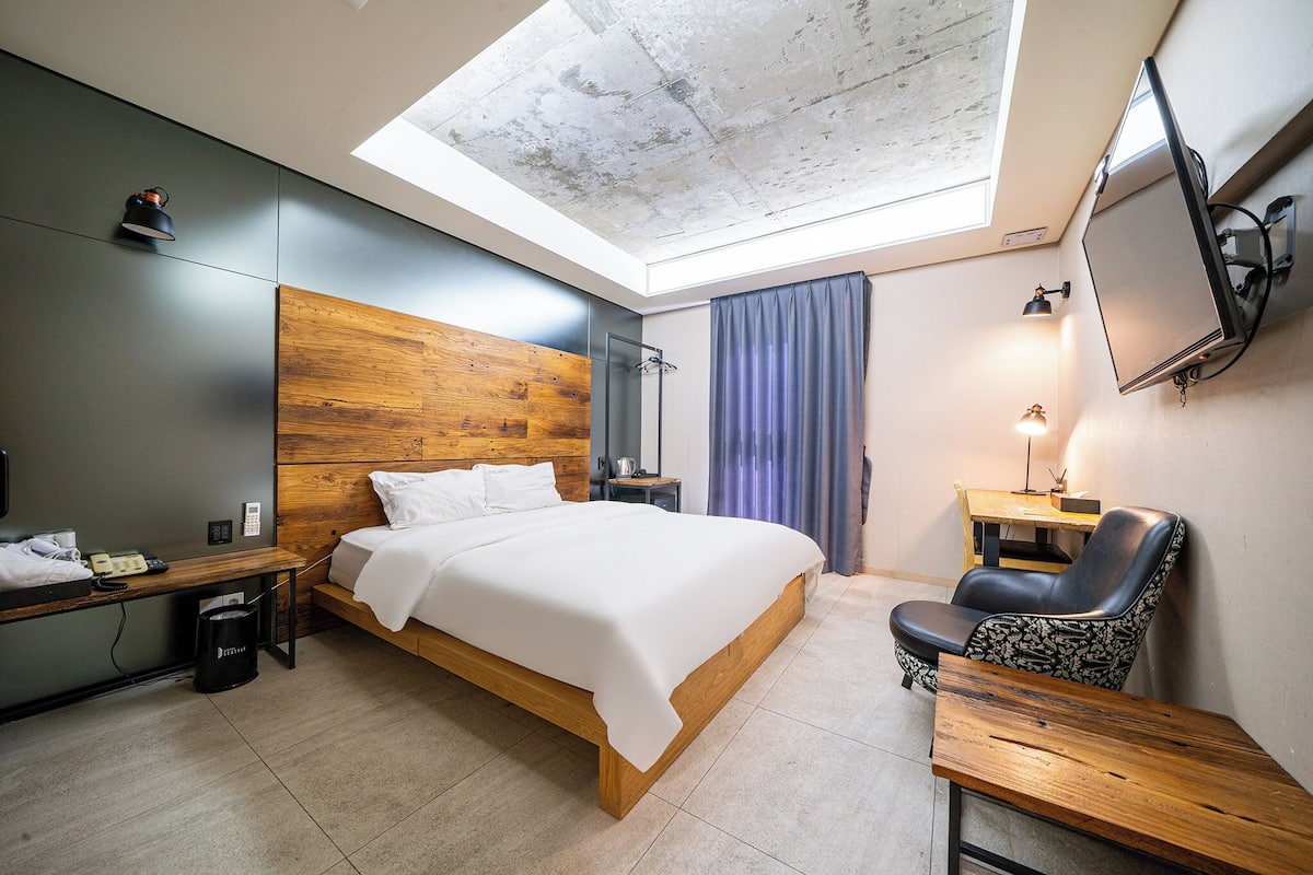 Ein modernes Hotelzimmer mit Dachfenster, einem Bett, einem Schreibtisch, einem Stuhl und einem Fernseher.