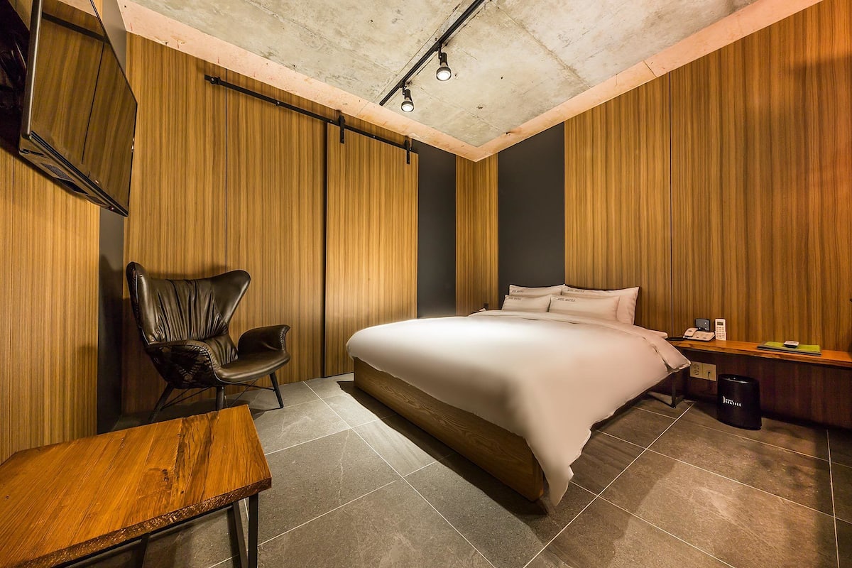Ein modernes Hotelzimmer mit einem großen Bett, einem Holztisch, einem Ledersessel und einem kleinen Tisch.