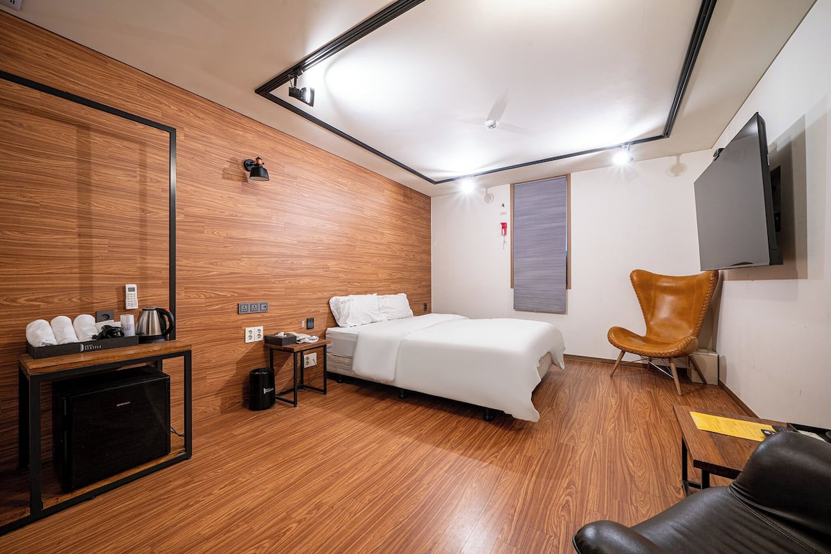 Ein modernes Hotelzimmer mit Holzboden, einem Bett, einem Schreibtisch mit Computer, einem Stuhl und einem an der Wand befestigten Fernseher.