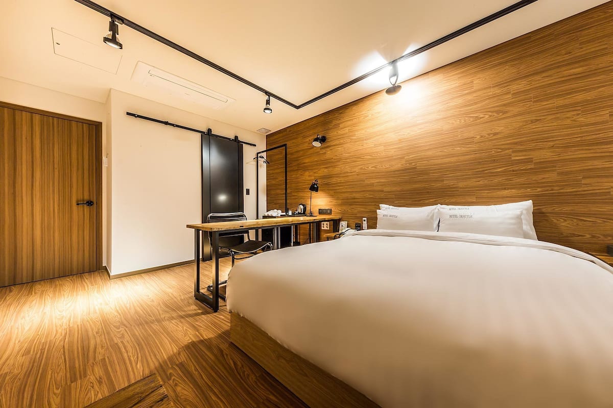 Ein Hotelzimmer mit Holzboden, einem Bett mit weißer Bettwäsche, einem Schreibtisch mit Stuhl und einem Fernseher.
