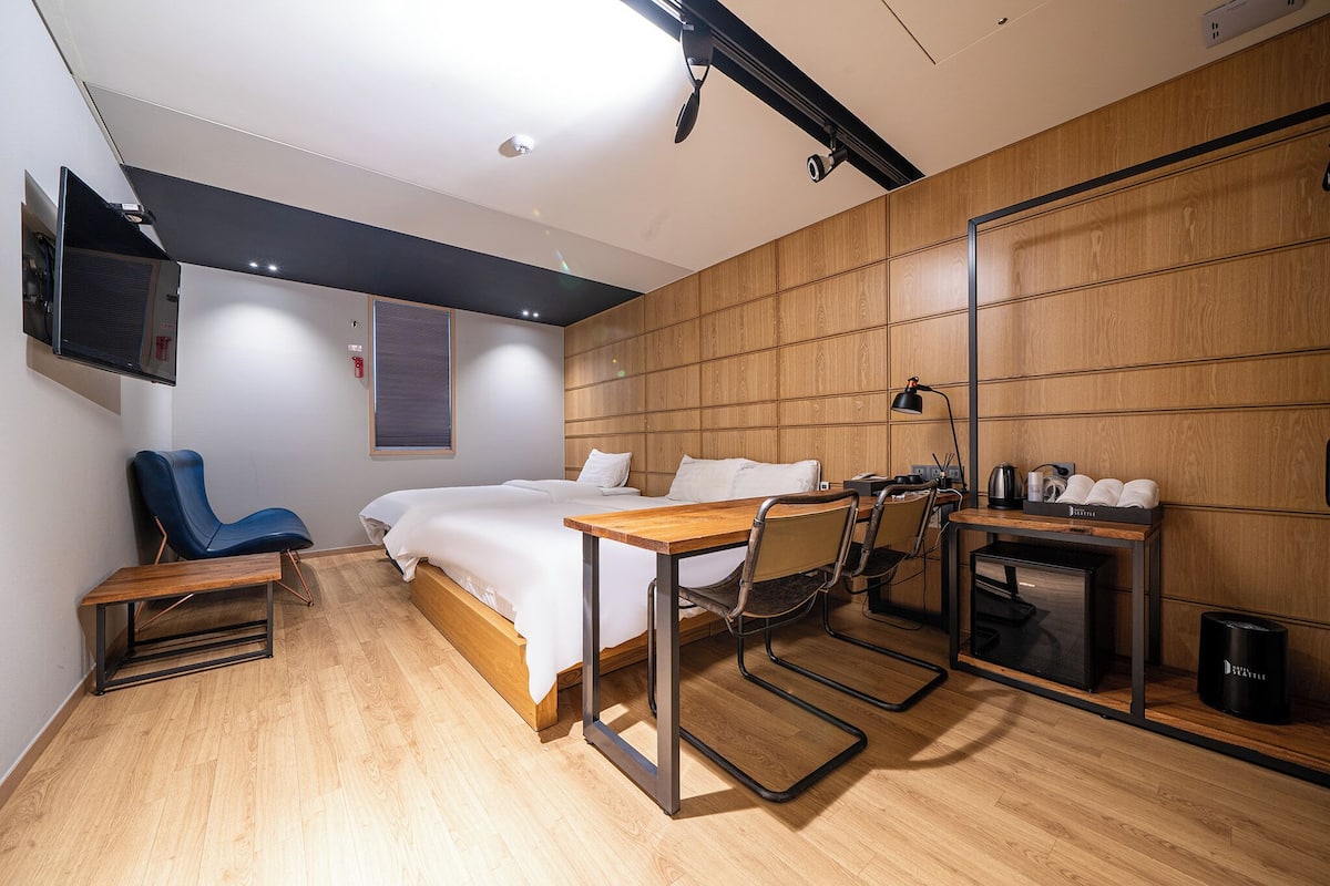 Ein modernes Hotelzimmer mit Bett, Schreibtisch, Stuhl und einer kleinen Küchenzeile.
