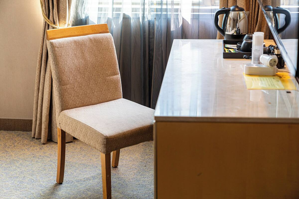 Ein Hotelzimmer mit einem beige bezogenen Sessel, einem Holztisch und einer Kaffeemaschine.