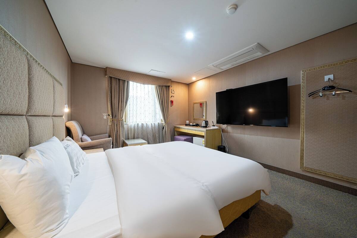 Ein Hotelzimmer mit einem großen Bett, einem Schreibtisch mit Stuhl, einem flachbildfernseher an der Wand und einem Kleiderständer.