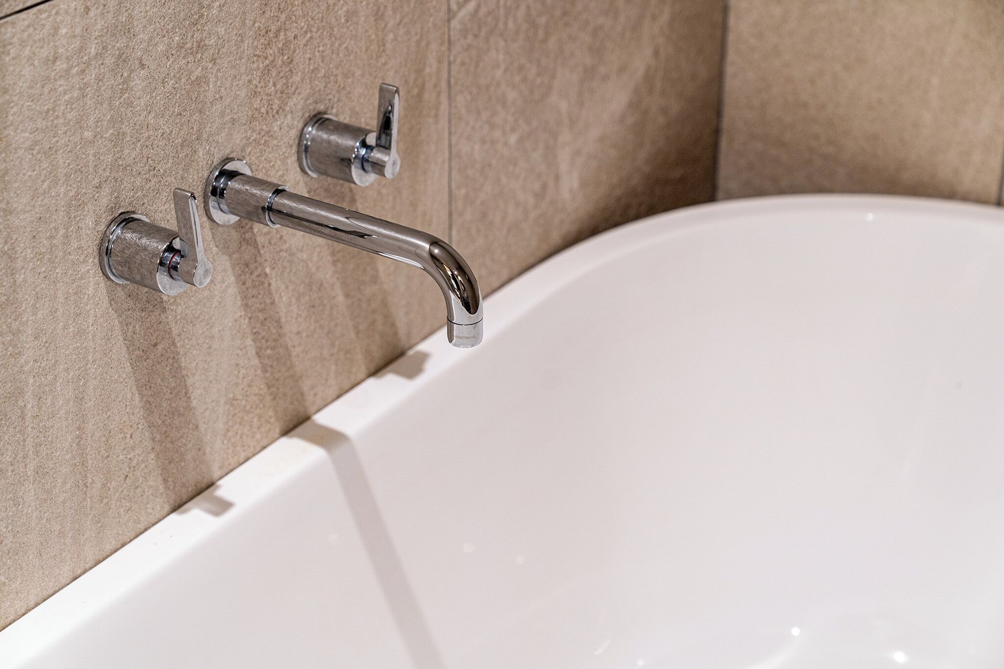 Una bañera blanca con accesorios de cromo frente a paredes con baldosas color crema.