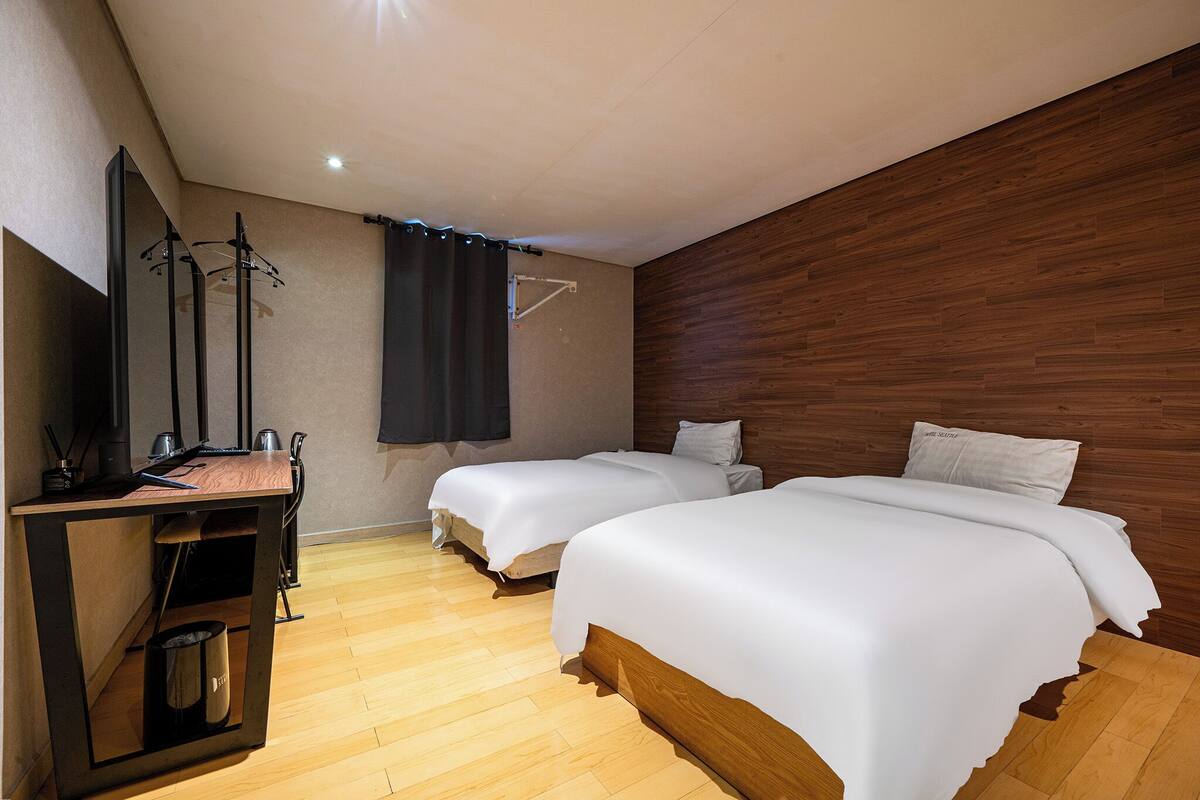 Ein Hotelzimmer mit zwei Betten, einem Holztisch, einem Spiegel und einem schwarzen Vorhang.