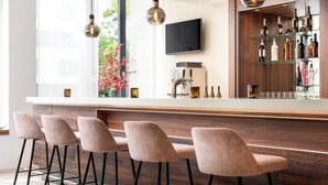 Eine moderne Bar mit einer langen Theke, Barhocker, einer Kaffeemaschine und einem an der Wand befestigten Fernseher.