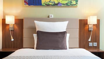 A hotel room with a large bed, two bedside lamps, a headboard, and a colorful abstract painting on the wall.