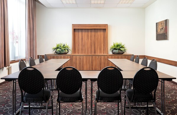 Un salón de conferencias con una larga mesa, sillas, plantas en macetas y un panel de pared de madera.