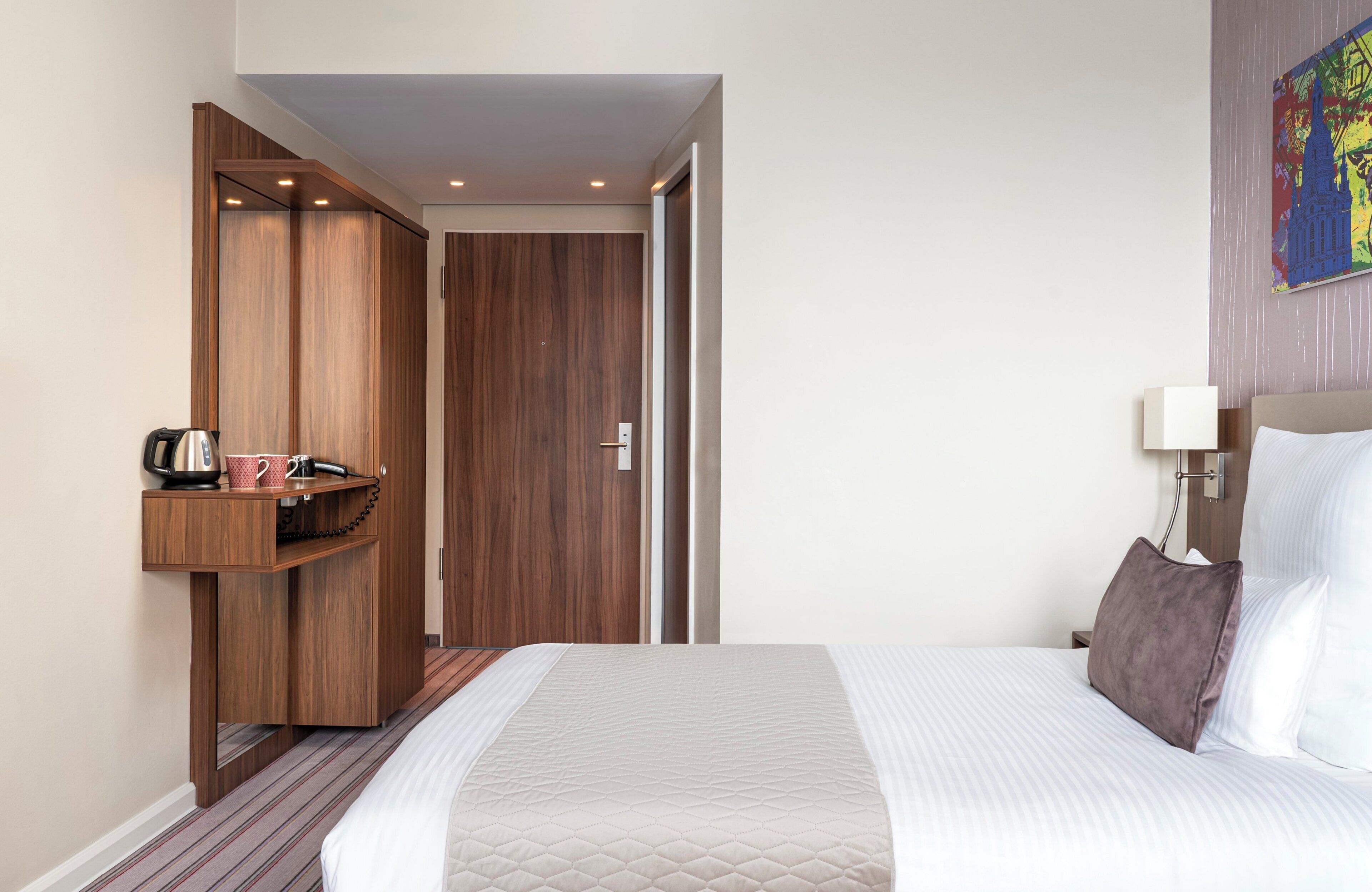 Ein Hotelzimmer mit einem Bett, einem Holzschrank, einem kleinen Tisch mit Wasserkocher und Tassen sowie einem Bild an der Wand.