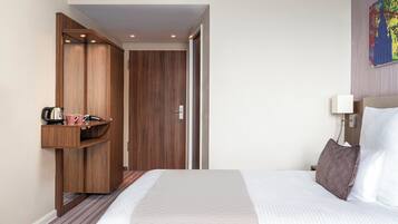 Ein Hotelzimmer mit einem Bett, einem Holzschrank, einem kleinen Tisch mit Wasserkocher und Tassen sowie einem Bild an der Wand.