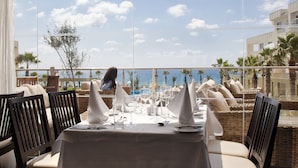 Comedor con una mesa preparada para dos, con vista a una piscina y palmeras, y una vista despejada del océano.