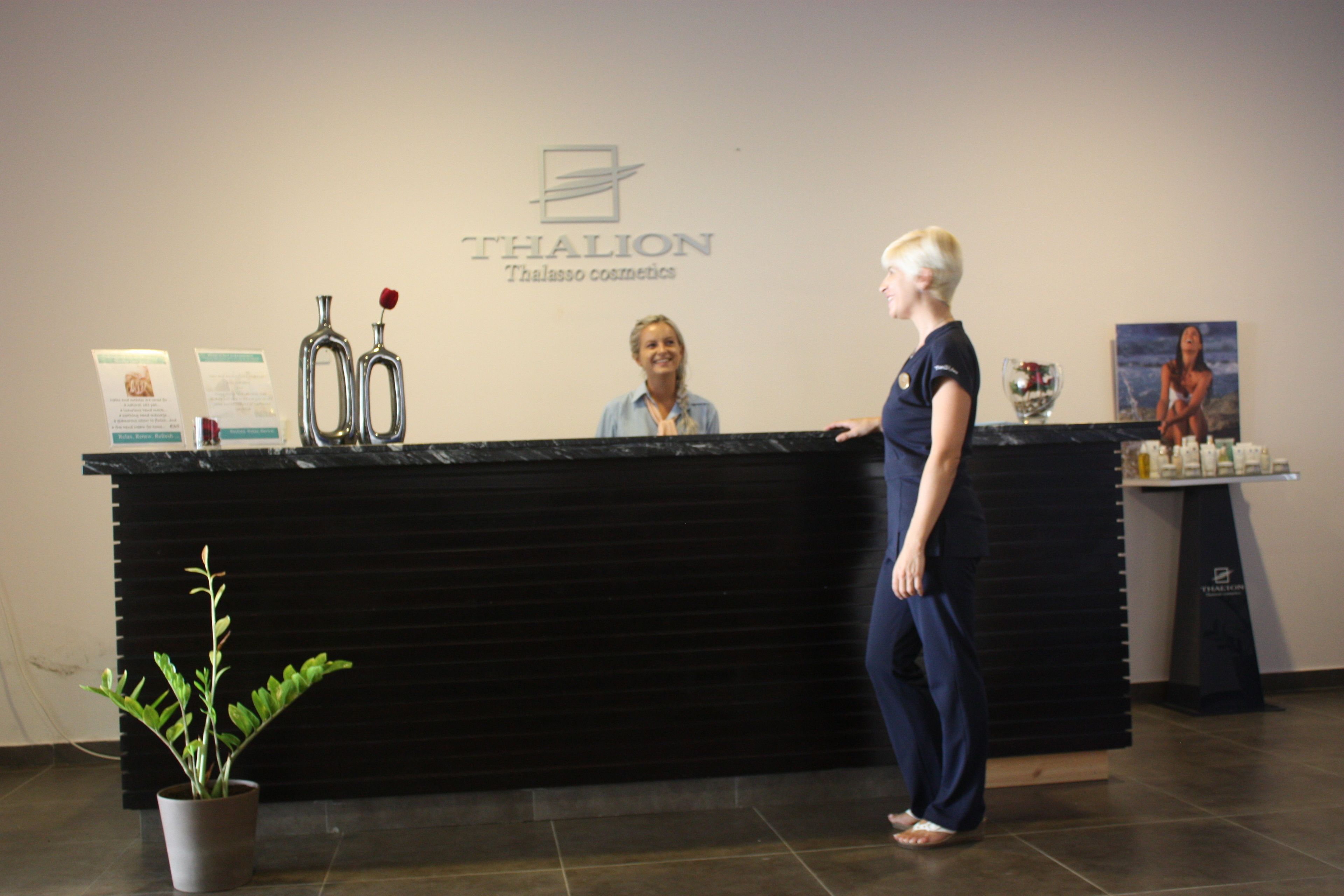 A reception desk with a logo, a potted plant, and a poster on the wall.