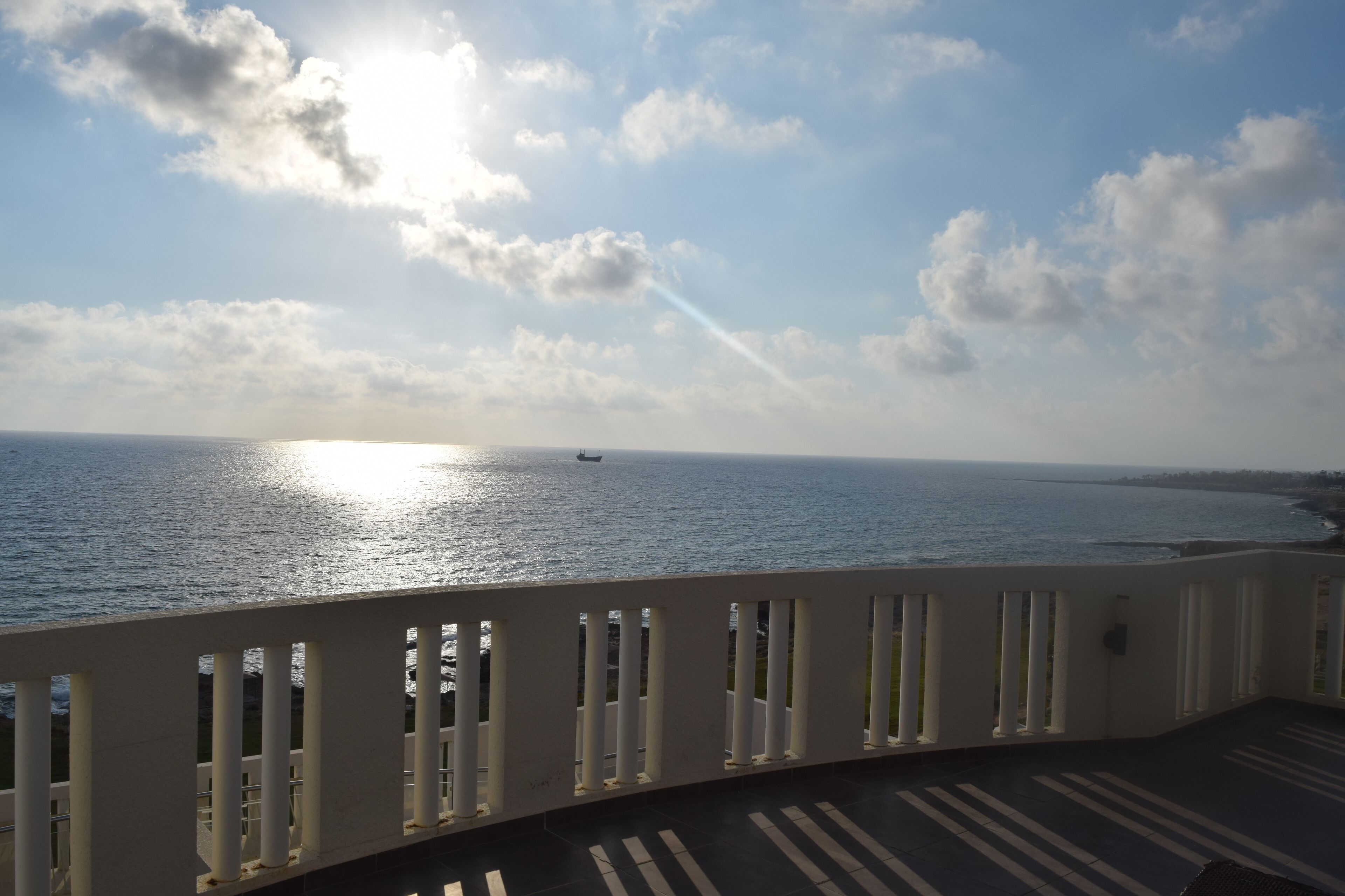 A balcony with a view of the sea and a ship in the distance.