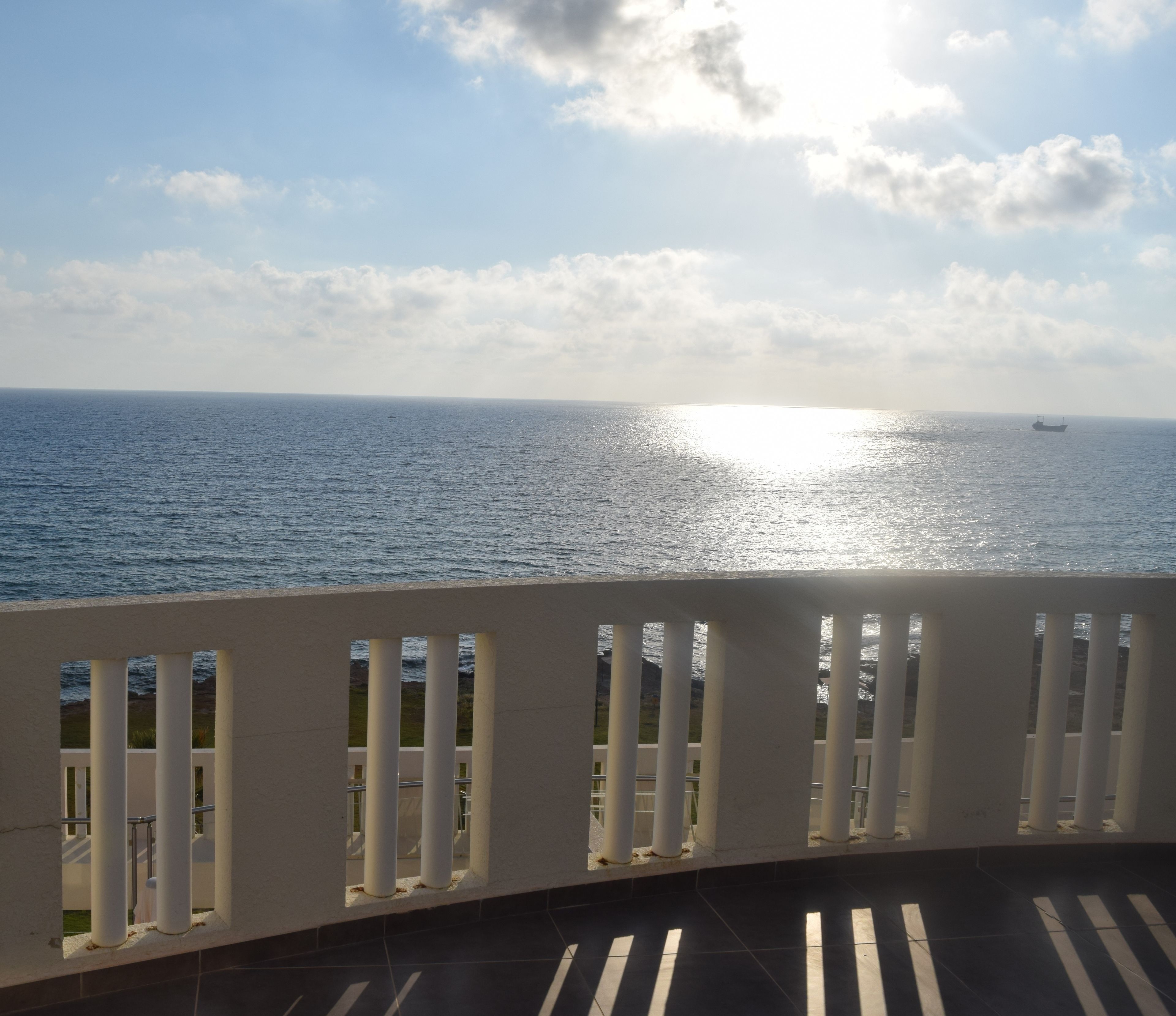 A balcony with a view of the sea and a ship in the distance.