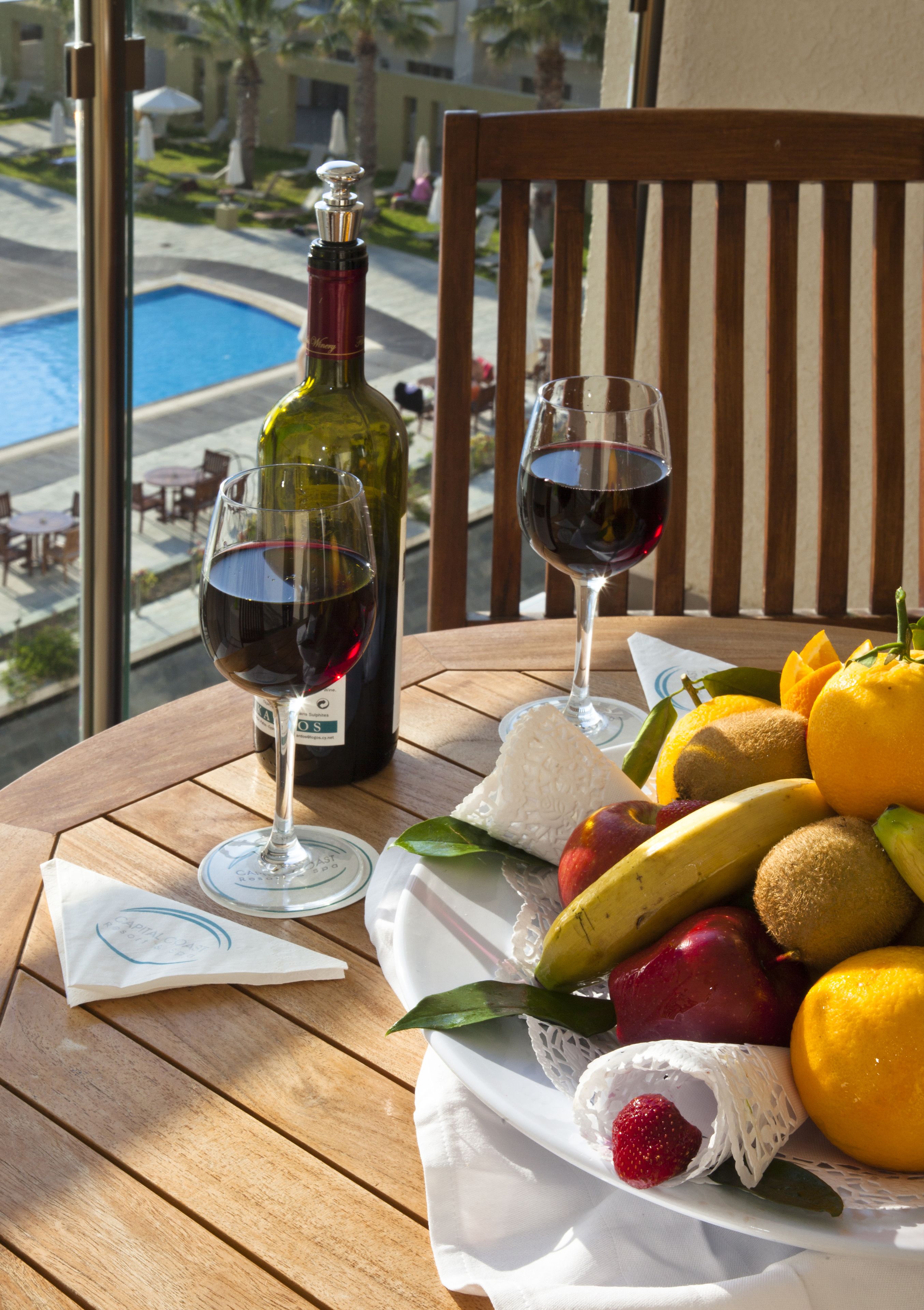 A table with a bottle of wine, two wine glasses, and a fruit basket.